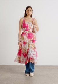 Robe midi fleurie en rose et crème, avec un corsage ajusté, une jupe à volants et une taille ceinturée. Associée à un jean bleu et des chaussures crème.