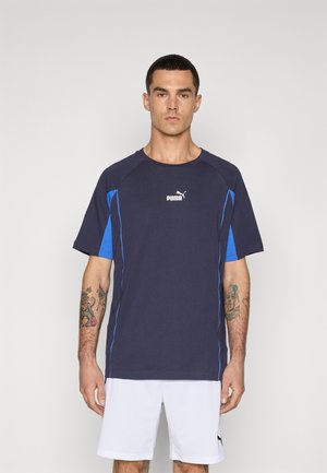 Navy blue athletic t-shirt with blue accents and Puma logo; short sleeves, round neckline, made of breathable fabric. White shorts worn.