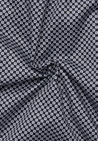 Gepatineerde stof met een zwarte achtergrond en witte geometrische vormen, wat een gestructureerde uitstraling creëert. Het materiaal is glad met een consistente weving.