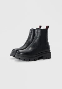 Bottines Chelsea en cuir noir avec une texture gaufrée crocodile, des panneaux latéraux élastiques et des semelles épaisses en caoutchouc noir. Comprend des languettes de traction en haut.
