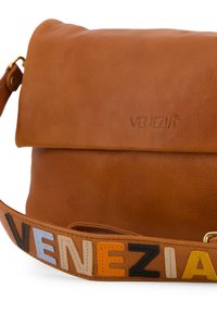 Hellbraune Lederhandtasche mit umklappbarem Deckel. Verstellbarer Riemen mit mehrfarbigen Blockbuchstaben, die "Venezia" buchstabieren. Glatte Textur, minimalistisches Design.