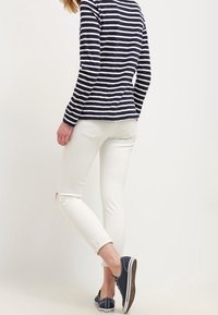 Gestreiftes Langarmoberteil in Marineblau und Weiß, kombiniert mit weißen, zerrissenen Skinny-Jeans und Marineblauen Sneakern, die ein lässiges Outfit präsentieren.