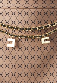 Tessuto marrone a fantasia con forme a rombo in blu navy. Due catene dorate con accenti neri e pendenti in metallo a forma di lettera pendono in modo prominente.