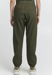 Olive green cotton jogger pants with elastic waistband and cuffs, featuring two back pockets and a crinkled texture. Paired with light sneakers.
