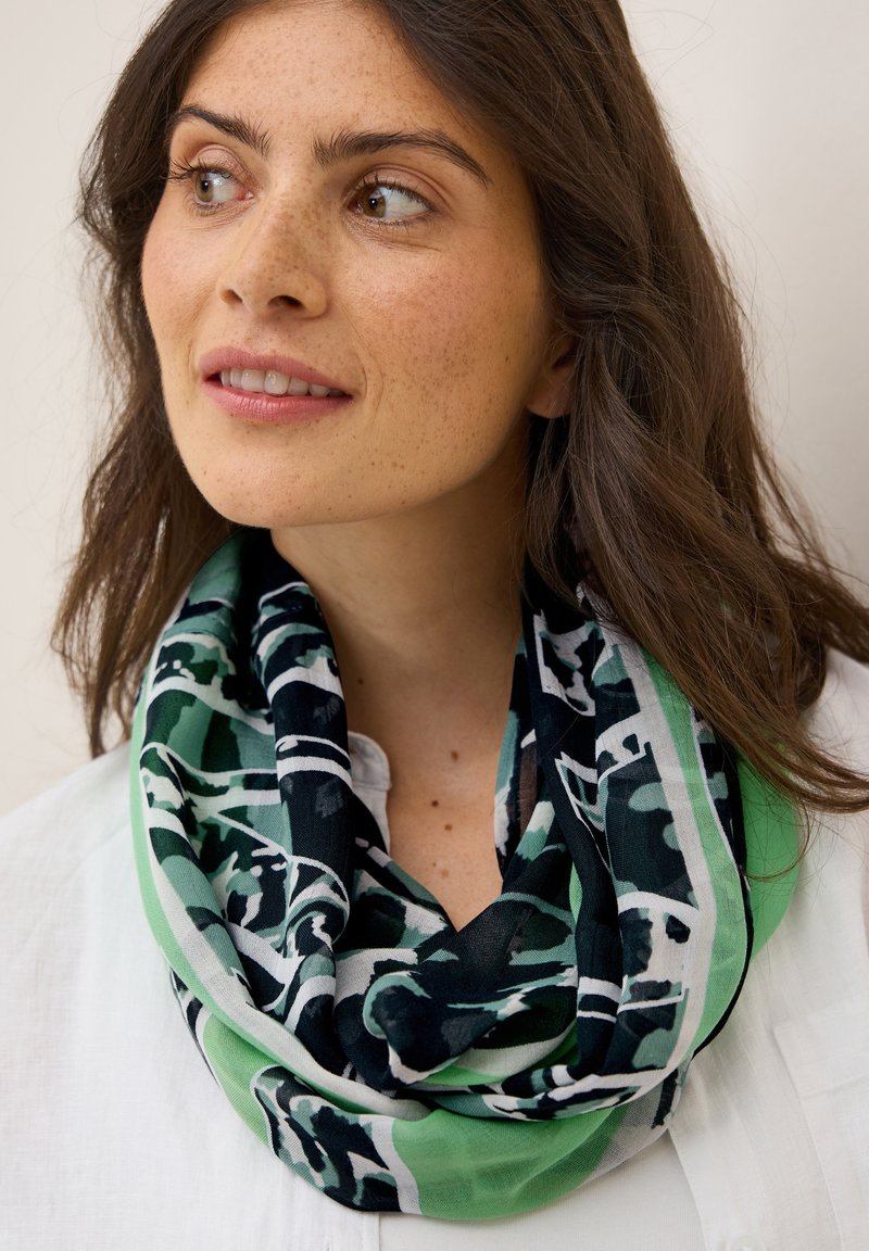Écharpe circulaire avec un motif abstrait vert, noir et blanc. Fabriquée en matériau léger, avec une texture douce et une finition lisse.