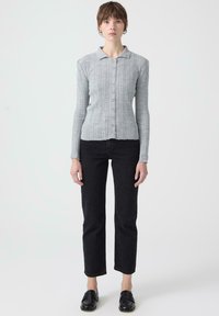 Szürke bordázott, hosszú ujjú felső, gallérral és elöl gombokkal, fekete, térdig érő nadrággal és fekete loaferekkel párosítva. Sima textúra, testhez álló kialakítás.