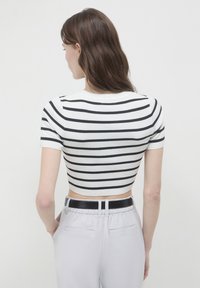Top corto bianco con strisce orizzontali nere, design aderente, maniche corte e scollo rotondo. Indossato con pantaloni grigi chiari dotati di una cintura nera.