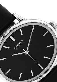 Montre analogique noire avec des index et aiguilles argentés. Boîtier argenté, bracelet en cuir noir. Design simple avec des caractéristiques minimalistes.