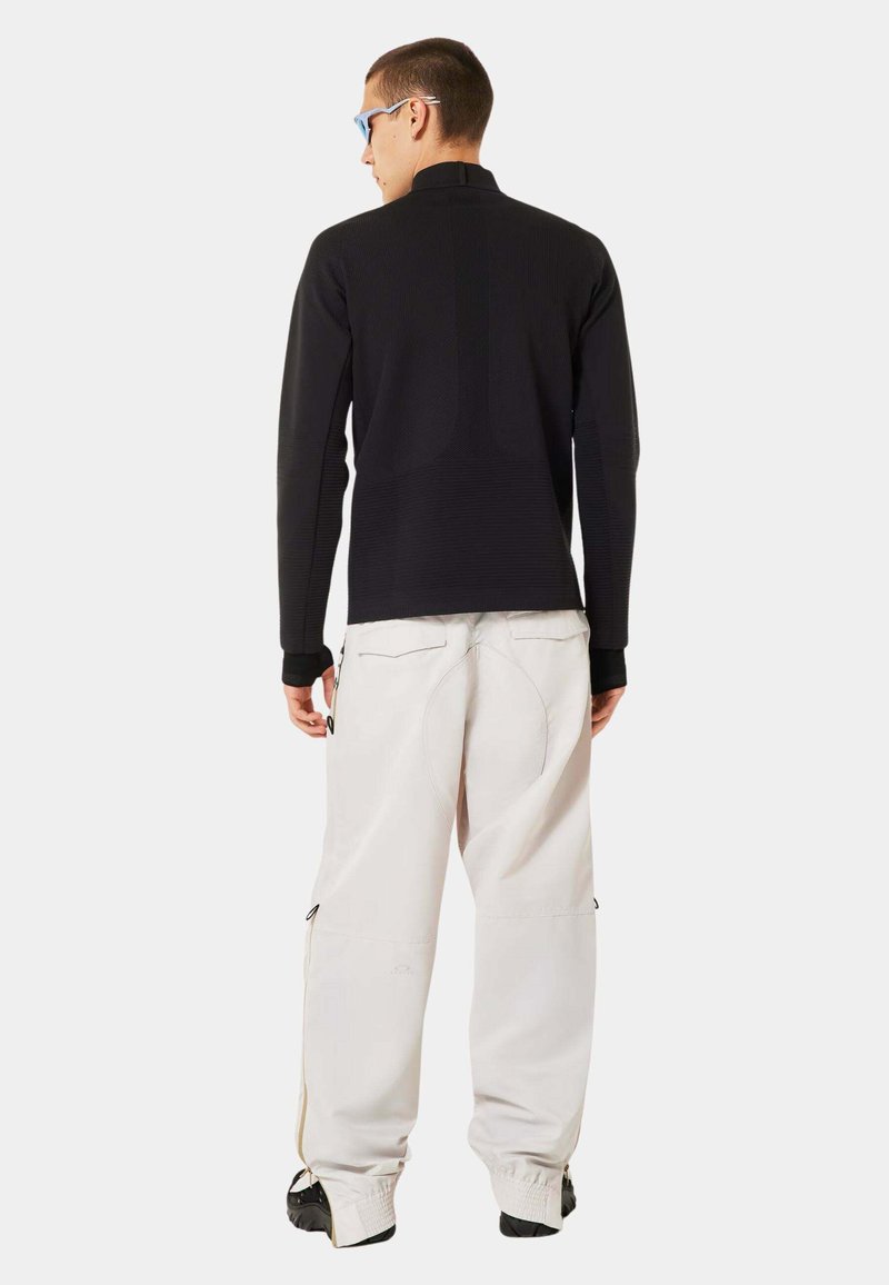 Black long-sleeve top with high collar and textured design; paired with loose-fitting, light gray pants featuring side zippers and pockets.