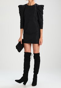 Černé šaty s nafouknutými rukávy a přiléhavým střihem. V kombinaci s černými semišovými kozačkami nad kolena a texturovanou černou kabelkou.