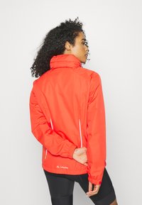 Red waterproof jacket with a high collar, elastic cuffs, and side zip pockets. Features reflective accents for visibility.