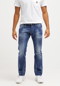 Blå denimjeans med rak skärning, ljus blekning, fem fickor och sömnadsdetaljer. Bärs med en vit t-shirt och vita sneakers.