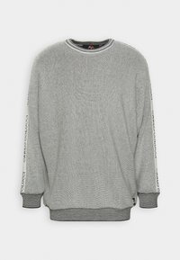 Felpa grigia lavorata a maglia con maniche lunghe, caratterizzata da un collo rotondo e un dettaglio con logo lungo le maniche. Lo sfondo semplice ne migliora la visibilità.