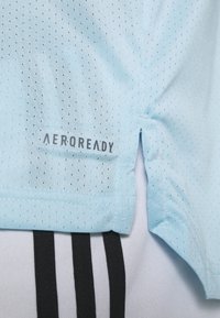 Camiseta atlética AEROREADY de color azul claro con tejido texturizado y acentos diagonales negros. Cuenta con aberturas laterales para mayor libertad de movimiento.
