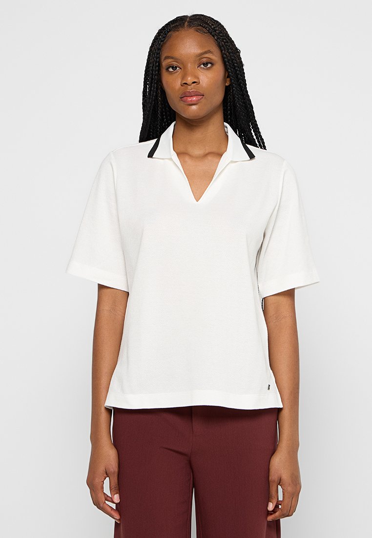 Polo shirt blanc à manches courtes avec un col noir en accent et une coupe décontractée. Fabriqué en tissu texturé avec un ourlet droit.