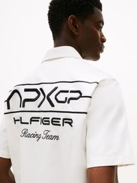 Bijela kratkosuknja košulja s crnim izvezenim grafičkim elementima koji prikazuju natpise "Racing Team" i "HLFINGER", s ovratnikom i teksturiranom tkaninom.