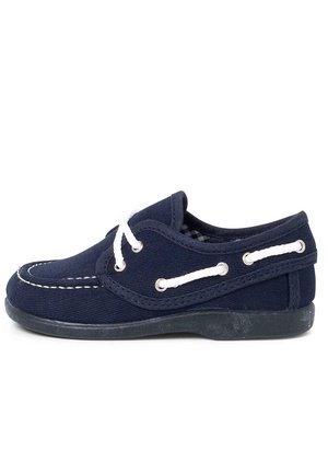 Marinblå kanvassko med vita snörningar, gummisula och kontrasterande sömmar. Har ögla på sidorna och en lågprofildesign.