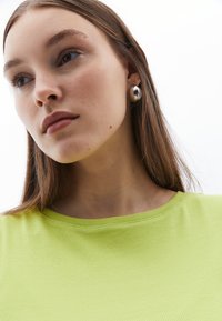 Grön ribbad t-shirt med rundad halsringning, bärs med silverfärgade studsörhängen. Slät textur med en tät silhuett.