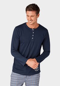 Marineblauw shirt met lange mouwen, een henley-halslijn, een knoopsluiting met vijf knopen en een logo-accent linksonder, gecombineerd met geruite broek.