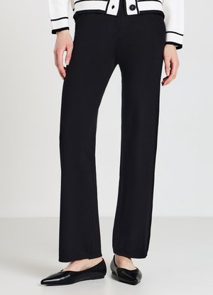 Schwarze, gerade geschnittene Hosen mit einer glatten Textur, hoher Taille und minimalen Nähten, kombiniert mit spitzen schwarzen Ballerinas.