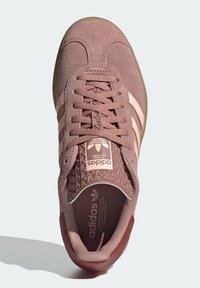 Baskets en daim rose clair avec des banderoles crème, accents texturés sur la languette et semelle en caoutchouc. Présente des lacets ronds et des détails cousus.