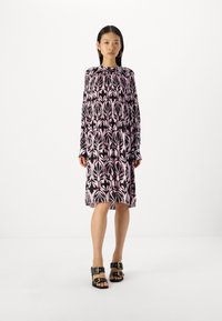 Schwarz und rosa bedrucktes langärmliges Kleid mit hohem Kragen und lockerer Passform; kombiniert mit klobigen schwarzen Sandalen mit goldenen Hardware-Akzenten.