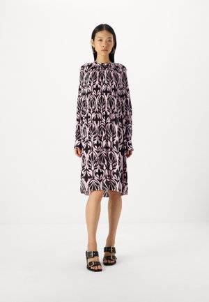 Black and pink printed long-sleeve dress with a high neck and loose fit; paired with chunky black sandals featuring gold hardware accents.