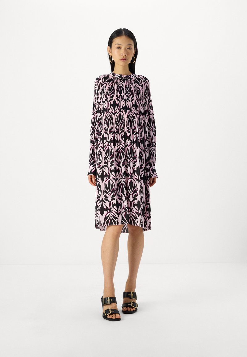 Schwarz und rosa bedrucktes langärmliges Kleid mit hohem Kragen und lockerer Passform; kombiniert mit klobigen schwarzen Sandalen mit goldenen Hardware-Akzenten.