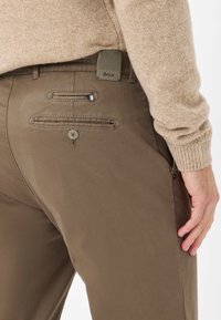 Pantaloni khaki dal design elegante, con due tasche posteriori con bottoni e un'etichetta in tessuto sulla vita. Materiale testurizzato.