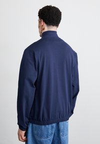 Sweatshirt azul-marinho com gola alta, punhos elásticos e cós, feito de um tecido suave. As costas são lisas, sem padrões ou adornos.