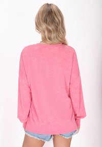 Felpa fucsia oversize con una texture morbida, polsini e orlo a costine. Presenta una vestibilità comoda e cuciture delle spalle leggermente abbassate.