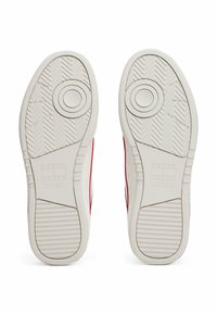 Weiße Gummisohlen von Sneakers mit strukturiertem Grip-Muster, das ein zentrales kreisförmiges Design und ein erhabenes Markenlogo aufweist, das in Rot umrandet ist.