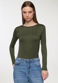 Oliwkowy sweter z długim rękawem, wykonany z gładkiego materiału, z okrągłym dekoltem, w połączeniu z jasnoniebieskimi dżinsami o wysokim stanie.
