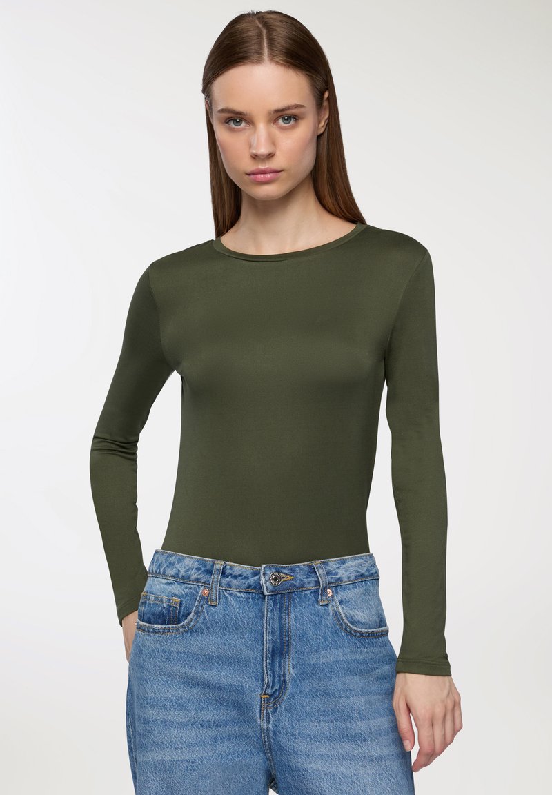 Oliwkowy sweter z długim rękawem, wykonany z gładkiego materiału, z okrągłym dekoltem, w połączeniu z jasnoniebieskimi dżinsami o wysokim stanie.