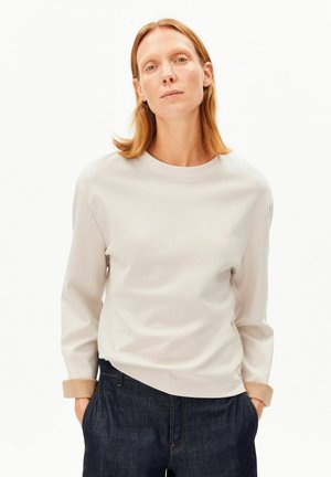 Sweat-shirt gris clair avec un col rond et des manches longues, doté d'un détail de revers roulé et associé à un pantalon en jean foncé.