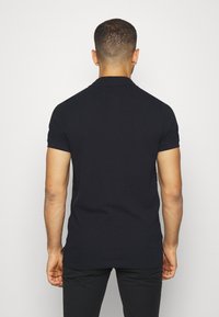 Camisa polo negra de manga corta, con cuello clásico y hombros sin costuras, hecha de una suave y lisa tela de algodón.