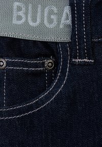 Jeans in denim scuro con un'etichetta in tessuto azzurro chiaro etichettata "BUGA"; presentano hardware argentato, cuciture bianche a contrasto e una tasca frontale.