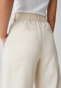 Beige hoge taillebroek met een elastische tailleband, voorzien van achterzakken en een glad, textuur stof. Ontwerp met een relaxte pasvorm.