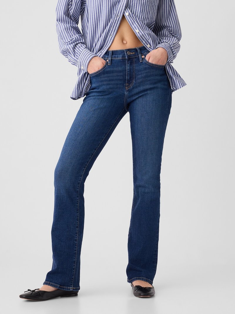 Dark blue denim flared jeans with a mid-rise waist, five-pocket design, and contrast stitching. Paired with a button-up striped shirt and flats.
