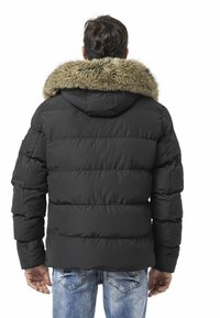 Schwarze Steppjacke mit einem Kapuzenbesatz aus Fell. Verfügt über ein gesteppte Design, gerippte Bündchen und eine lockere Passform. Wird über blauen Jeans getragen.