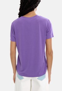 Fioletowa koszulka krótki rękaw z miękkiego materiału, z okrągłym dekoltem, o luźnym kroju i gładkiej fakturze. Zaprezentowany widok z tyłu.