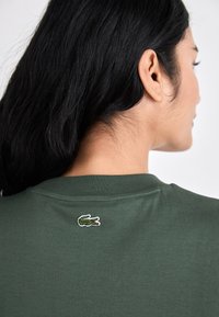 Grønn bomull t-skjorte med ribbet rund hals og brodert krokodille-logo på baksiden. Glatt tekstur med korte ermer.