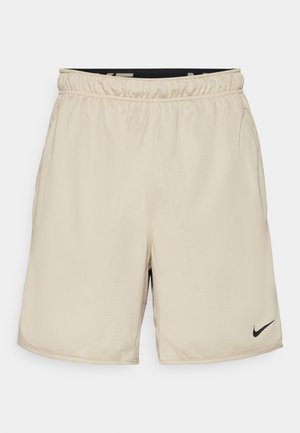 Beige idrettsshorts laget av lett materiale med elastisk liv, med en liten svart Nike-logg nederst til høyre.