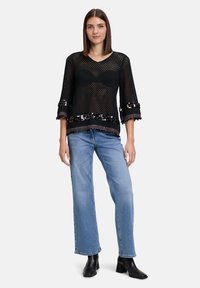 Schwarzes Netzoberteil mit Dreiviertelärmeln, das einen Paillettensaum am Saum hat. Getragen mit hellblauen geraden Jeans und schwarzen Knöchelstiefeln.