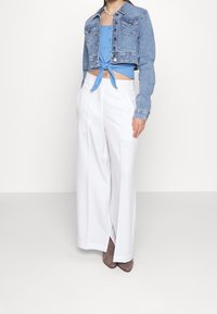 Denim cropped jack met twee borstzakken, blauwe cropped top met knoopdetail, en witte wijde broek met grijze haklaarzen.
