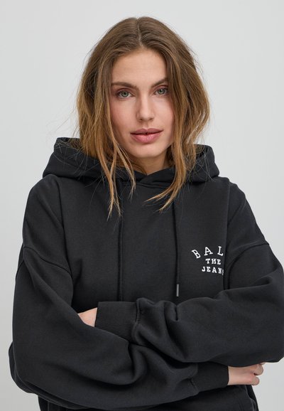 Černá mikina s kapucí, šňůrkou a přední kapsou. Obsahuje bílo vyšívaný text "BAL THE JEANS." Měkká textura a uvolněný střih.