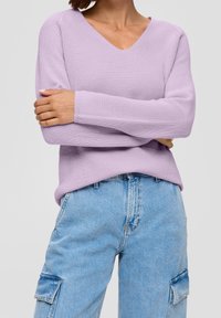 Pull en maille côtelée lilas avec un col en V et des manches longues, associé à un jean cargo bleu clair avec des poches latérales.
