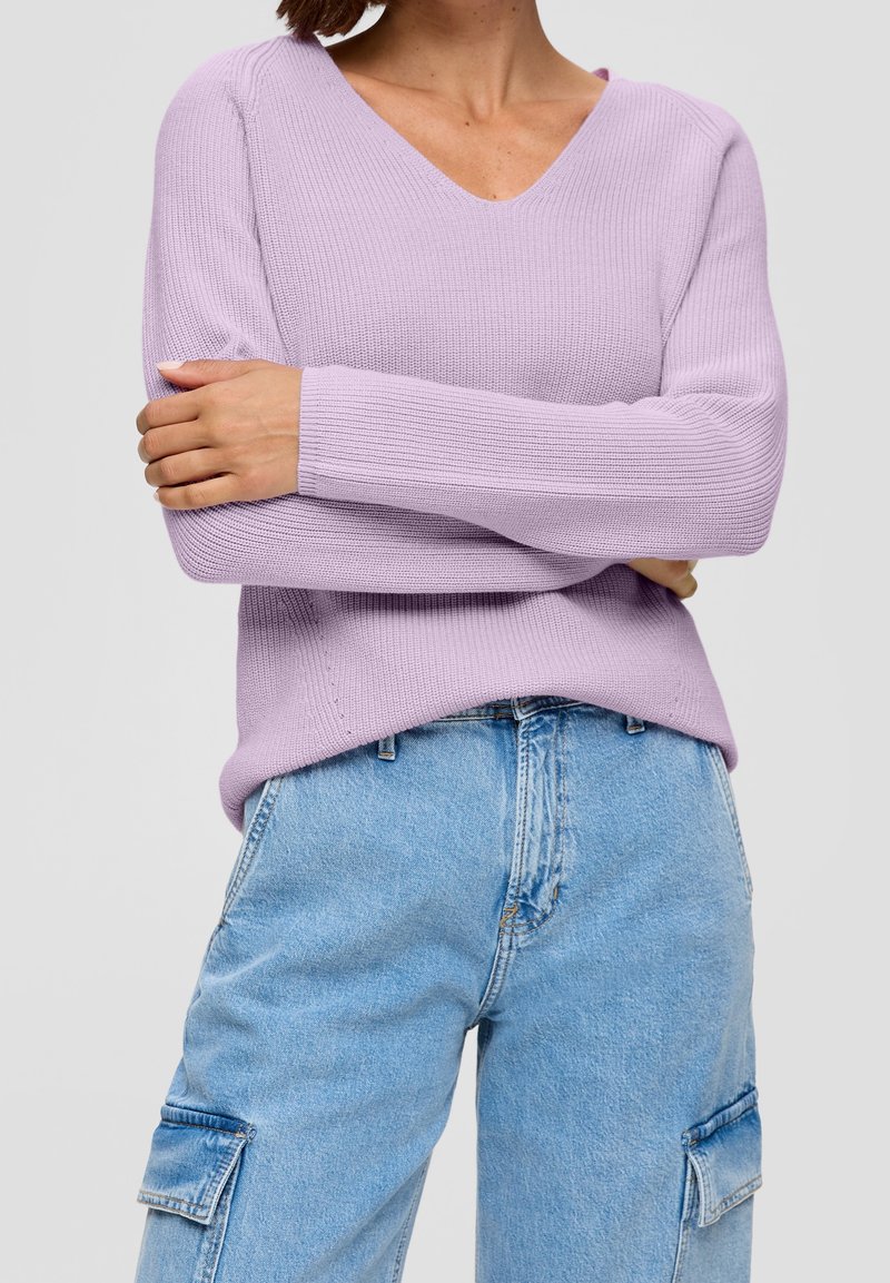 Pull en maille côtelée lilas avec un col en V et des manches longues, associé à un jean cargo bleu clair avec des poches latérales.