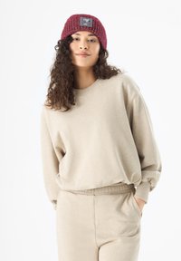 Beige sweatshirt and matching pants with a relaxed fit; ribbed burgundy knit beanie features a patch with a character design.