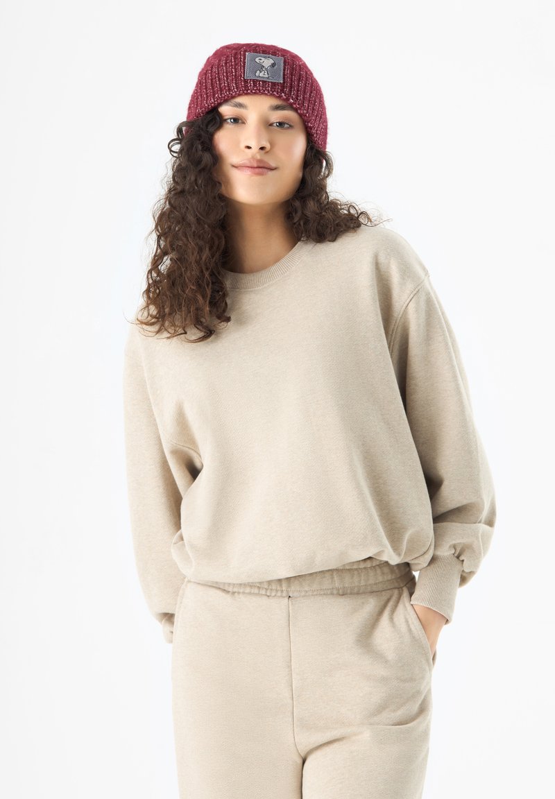 Beige sweatshirt and matching pants with a relaxed fit; ribbed burgundy knit beanie features a patch with a character design.